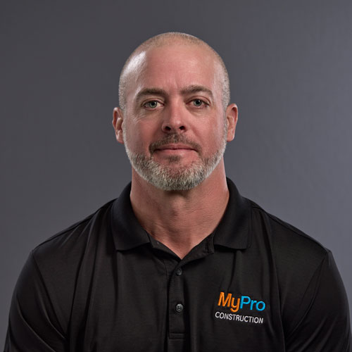A man with a shaved head and beard wearing a black MyPro Construction polo shirt sits in front of a plain gray background.