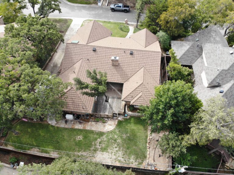 Aerial view of a house with a brown stone coated steel roof replacement, wooden deck, and backyard surrounded by trees, suitable for a home improvement project.