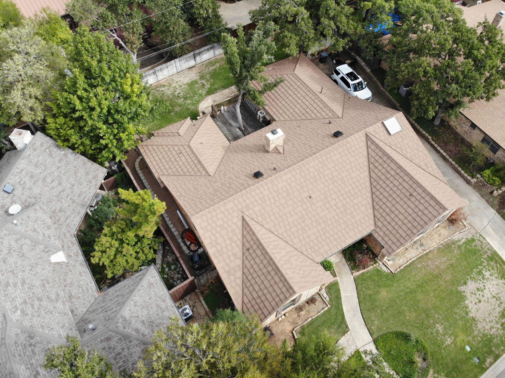 Aerial view of a residential house in Arlington, Texas with a brown stone-coated steel roof undergoing a property transformation, surrounded by trees and a lawn.
